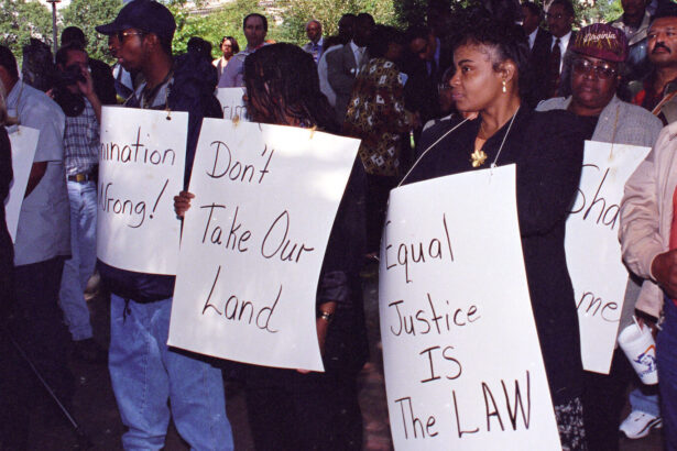 photo of male and female Black farmers at a protest, holding signs that read "Discrimination is wrong," "Don't take our land," and "Equal justice is the law"