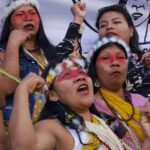 A group of women with headdresses and red face paint shout together