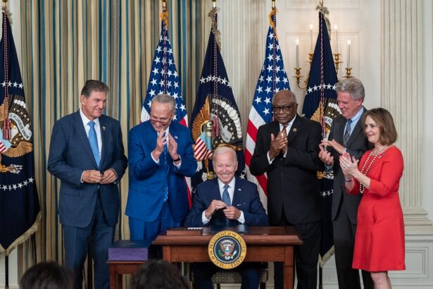 President Biden sits at a desk surrounded by other politicians and signs a bill