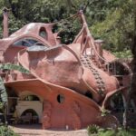 the exterior of an organically-shaped home with circular windows, circular details that resemble suckers on octopus tentacles, and varying convex slopes of terra-cotta tones