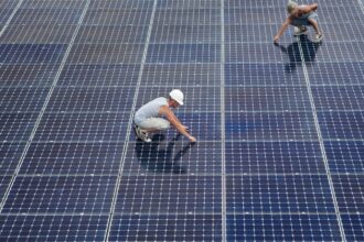 Two men installing solar panels on rooftop.