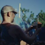 a white man in a hat holds up a trophy while standing in a dumpster