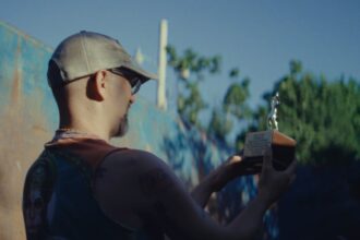 a white man in a hat holds up a trophy while standing in a dumpster