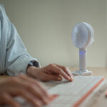 A person types on a keyboard next to a small fan