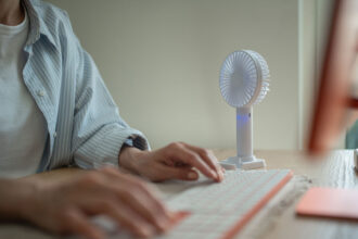 A person types on a keyboard next to a small fan