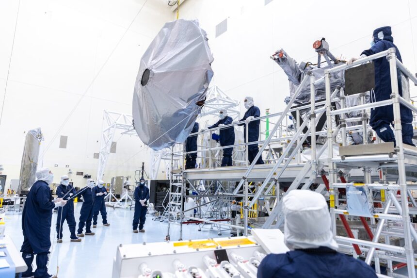 Technicians in blue suits and white caps installing antenna on spacecraft