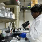 A woman in a scientific laboratory, wearing a lab coat and gloves.