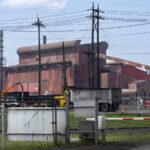 A red rusting plant sits next to an electric line