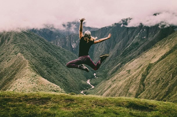 A woman jumping high in the green and lush mountains.