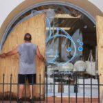 A man places plywood over an arched window on the storefront for a fish store in Florida