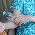 A woman in a blue shirt holds a cold water bottle to her arm