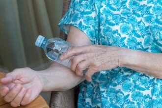 A woman in a blue shirt holds a cold water bottle to her arm