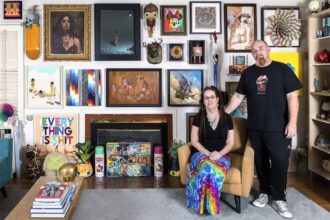 a portrait of gallerists Shawn and Andrew Hosner in their home, standing in front of a wall of paintings and artworks