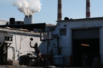 A young person plays basketball behind a truck stop restaurant as emissions spew out of a large stack nearby at the coal-fired Morgantown Generating Station on the Potomac River in Newburg, Maryland.