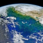 Satellite composite image of the California coast and Pacific Ocean with varying colors of blues and greens where there are phytoplankton blooms. The curve of the Earth can be seen at the top of the image