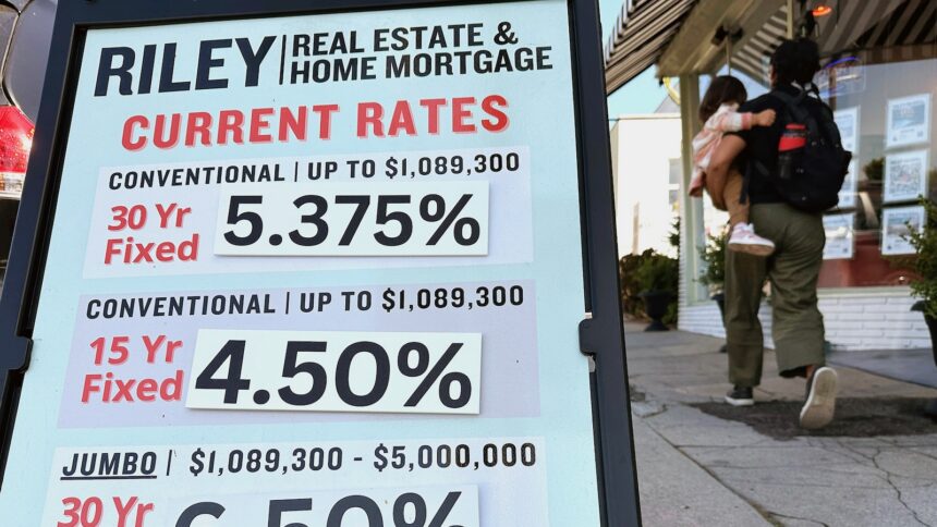 Pedestrians walk by a sidewalk sandwich board providing the latest interest rates for home mortgages.