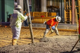 Two workers wearing hard hats spread concrete