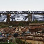 a procession of train cars above a village depicts 3 large black and white photographs of expressive faces