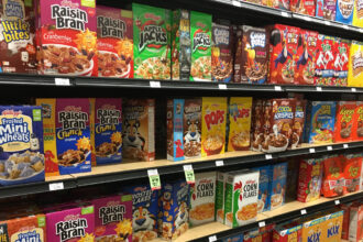 Grocery store shelves, filled with colorful cereals, like Raisin Bran, Apple Jacks, Pops, and Froot Loops.