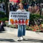 Scientist holding a sign saying "Scientists Say: End Fossil Fuels"