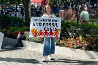 Scientist holding a sign saying "Scientists Say: End Fossil Fuels"