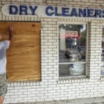 A man boards up the window of a dry cleaning business.