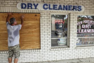 A man boards up the window of a dry cleaning business.