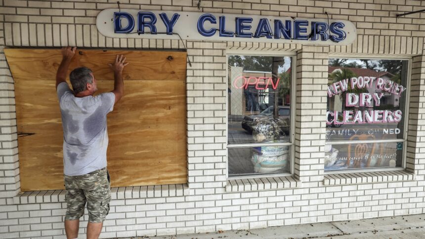 A man boards up the window of a dry cleaning business.