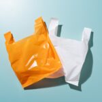 Two plastic bags, one orange and one white, lie flat against a blue background.