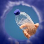 Photograph shot looking up from inside a recycling bin as a person's hand is about to drop a plastic bottle into the opening