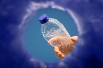 Photograph shot looking up from inside a recycling bin as a person's hand is about to drop a plastic bottle into the opening