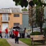 A group of people walk on a sidewalk in front of a two story apartment building