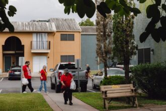 A group of people walk on a sidewalk in front of a two story apartment building