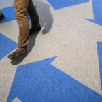 A large blue chasing arrows recycling symbol on the floor, with two people walking on top of it.