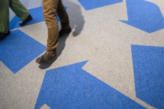 A large blue chasing arrows recycling symbol on the floor, with two people walking on top of it.