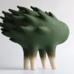 an abstract ceramic sculpture of a green form with a flame-like texture on its back, with four legs