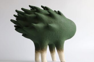 an abstract ceramic sculpture of a green form with a flame-like texture on its back, with four legs