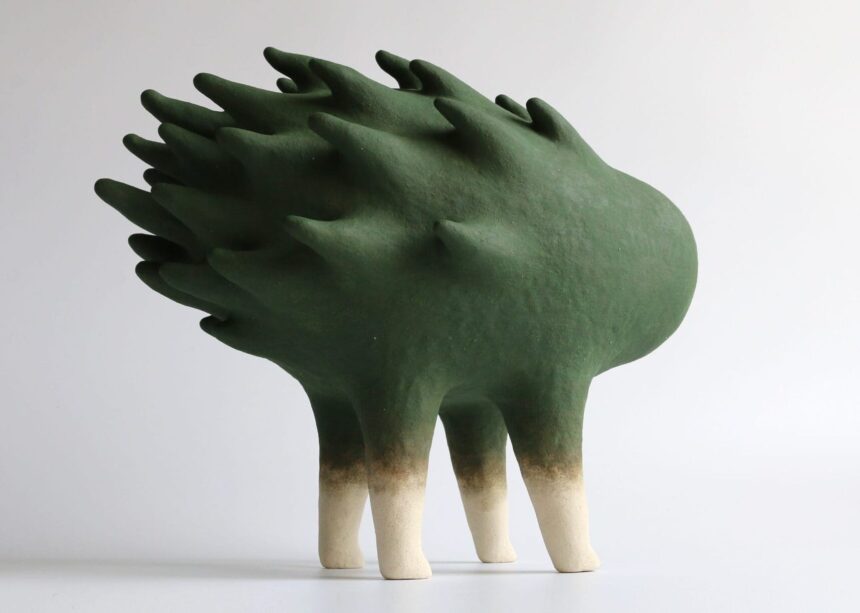 an abstract ceramic sculpture of a green form with a flame-like texture on its back, with four legs