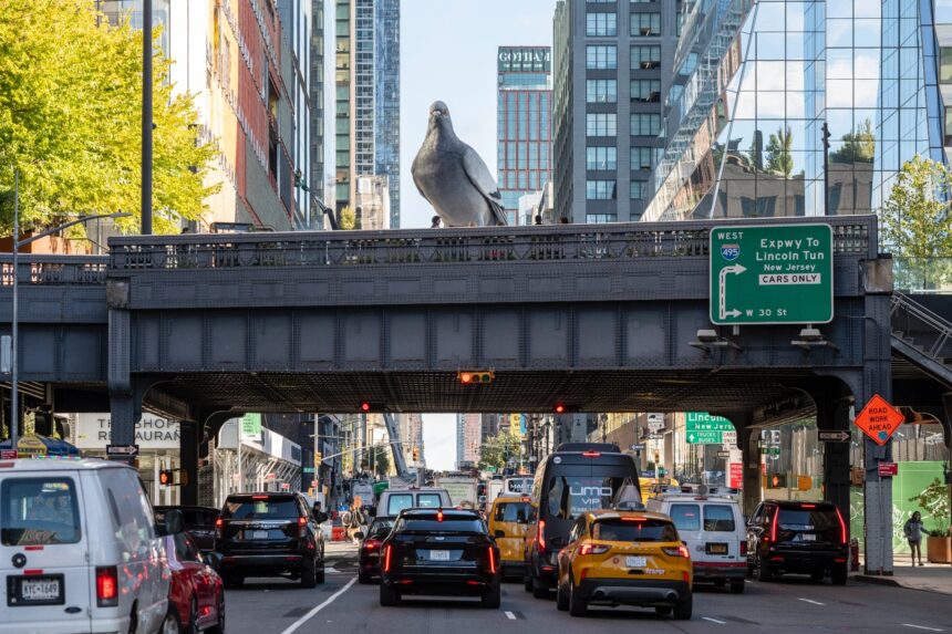 a large aluminum pigeon sculpture on a walkway above a road