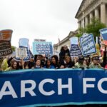 A group of people stand with signs behind a March for Science banner on a street in DC