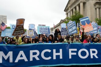 A group of people stand with signs behind a March for Science banner on a street in DC