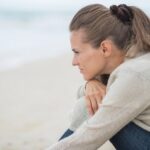 A sad woman sitting on a beach thinking.