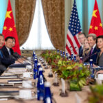 photo of a 2023 meeting between the US and China; President Xi Jinping and members of his staff sit on the left side of the table and President Joe Biden and members of his staff sit on the right side; flags of both countries are in the background