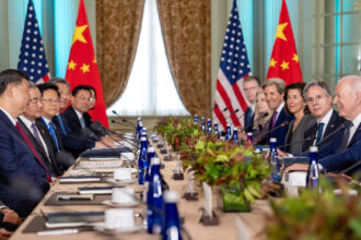 photo of a 2023 meeting between the US and China; President Xi Jinping and members of his staff sit on the left side of the table and President Joe Biden and members of his staff sit on the right side; flags of both countries are in the background