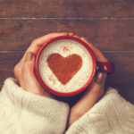 A woman holding a mug of coffee with a heartshape in the foam.