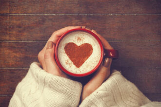 A woman holding a mug of coffee with a heartshape in the foam.