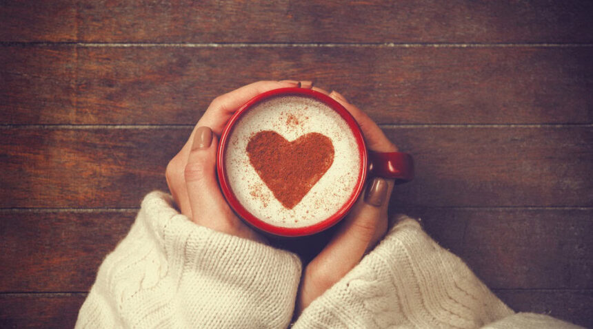 A woman holding a mug of coffee with a heartshape in the foam.