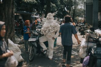 a photograph of a person standing next to a motorbike, wearing a handmade costume made from white plastic yarn, with woven arms and legs and a torso-head design that resembles coral textures