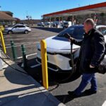 A middle-aged man prepares to plug his electric vehicle into a public charger at a filling station on the Massachusetts Turnpike.