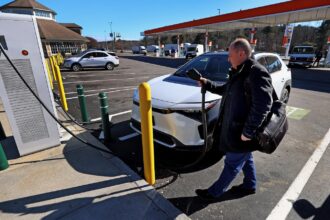 A middle-aged man prepares to plug his electric vehicle into a public charger at a filling station on the Massachusetts Turnpike.